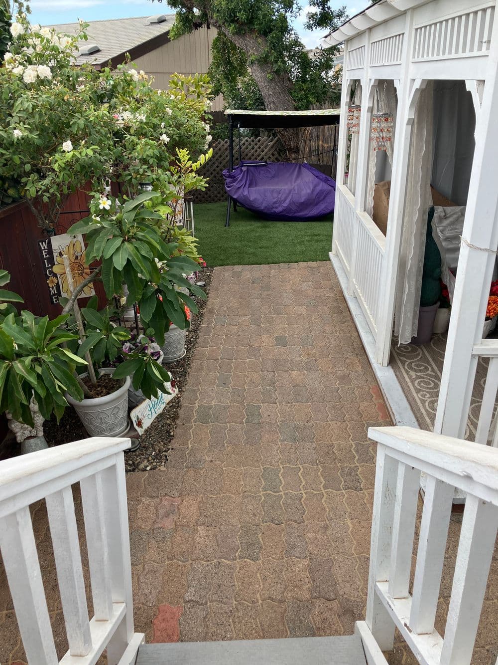 Pathway leading to a gazebo with potted plants and a hammock in a garden setting.
