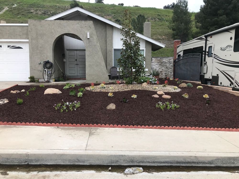 Landscaped front yard with rocks, plants, and decorative stones in a residential area.