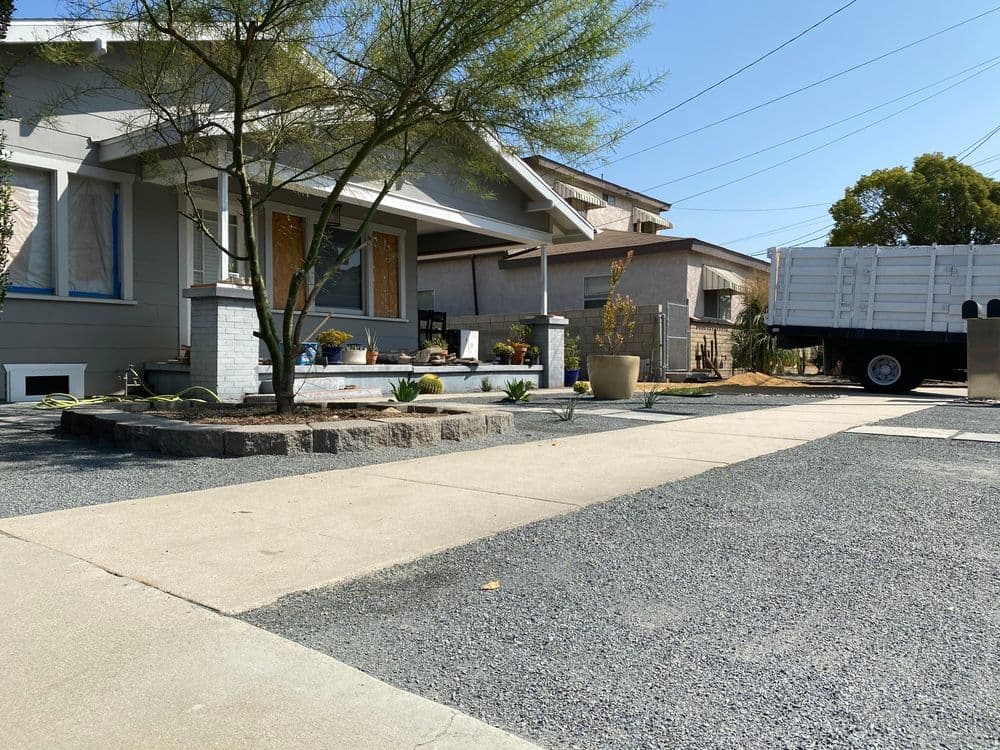 Front yard of a house with gravel driveway, planter, and nearby delivery truck.